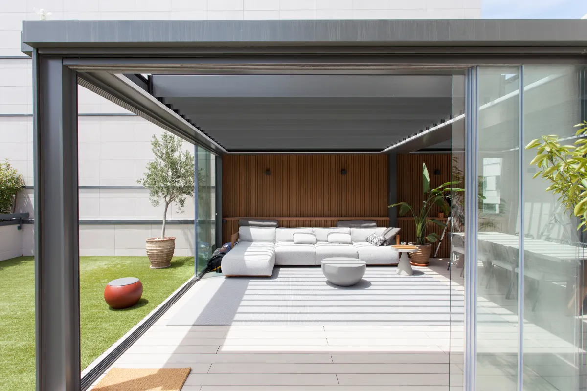Pérgola bioclimática retráctil NUMA en ático — control solar y ventilación natural Terraza de ático con pérgola bioclimática retráctil NUMA, lamas abiertas para ventilación natural y zona de estar exterior con sofá modular
